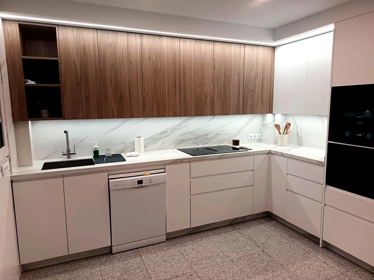 Cocina en L de madera y blanco con isla en mármol y luz LED bajo mueble